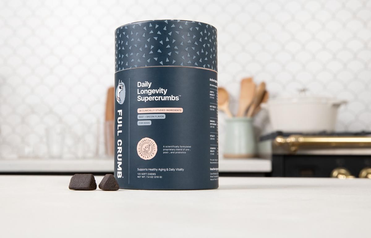 A jar of Full Crumb Daily Longevity Supercrumbs on a kitchen counter, with two soft chews beside it
